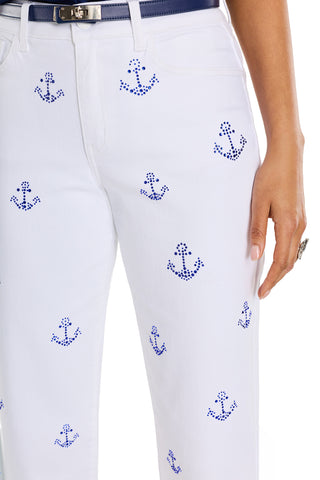 A person wearing the Kelsey Cropped Jean - Crystal Anchors, featuring white cropped jeans with blue anchor patterns and a navy belt. Only their torso and part of one arm are visible.