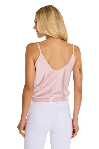A woman with long blonde hair is shown from the back wearing the Yara Silk Camisole - Blush with adjustable straps and white pants, standing against a white background. She has a tattoo on her left upper arm.
