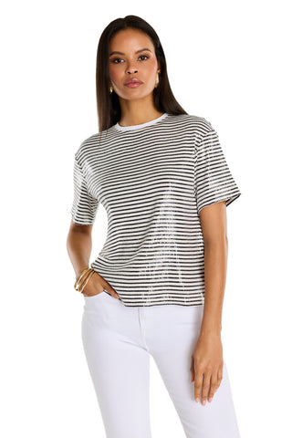A woman stands facing forward, wearing the Miranda Sequin T-Shirt in navy stripe and white pants. She has long straight hair, gold hoop earrings and bracelets, with a neutral expression against a plain white background.