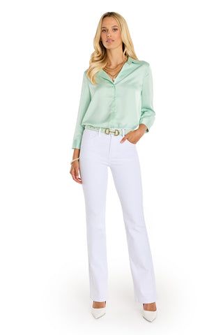A woman with long blonde hair poses against a white background wearing the Sara Silk Blouse in Mint, paired with white high-waisted belted pants and heels. She completes her polished look with layered necklaces and bracelets.