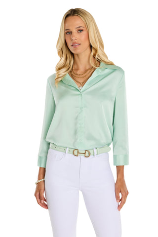 A woman wearing the Sara Silk Blouse - Mint, featuring a polished silhouette and three-quarter sleeves, tucked into high-waisted white pants with a matching mint belt. She accessorizes with layered gold necklaces and a bracelet.