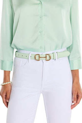 A person in a light green button-up shirt tucked into white jeans, accessorized with the Bettie Belt - Mint featuring a gold buckle and a pearl bracelet on their left wrist.