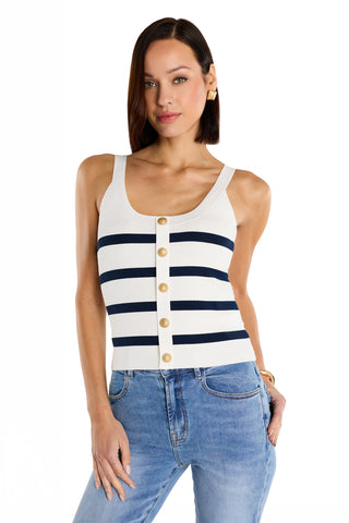 A woman with straight brown hair and a relaxed expression stands against a white background, wearing the Ruth Button Tank - Navy Stripe with signature gold dome buttons, paired with light blue jeans.