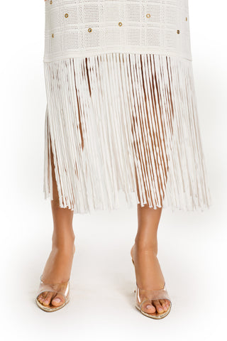 A person wearing the Romy Embellished Dress - Pearl, featuring a white grid pattern and long fringe at the hem, paired with clear high-heeled sandals, stands against a white background.