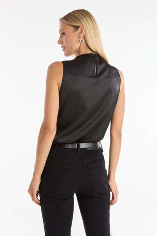 A woman with long blonde hair models the Mara Silky Top in black—a sleeveless mock neck style—paired with black jeans, standing with her back and head slightly turned against a white background.