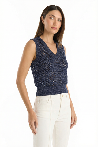 A woman with straight brown hair wears the Addison Sequin Crochet Top - Navy and high-waisted white pants, standing against a plain white background and looking at the camera with a neutral expression.