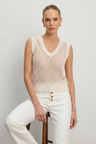 A woman sits on a stool against a plain background, wearing the Addison Sequin Crochet Top in Pearl and high-waisted white pants with three buttons. Her hair is slicked back, and she accessorizes with gold hoop earrings for a chic resort look.