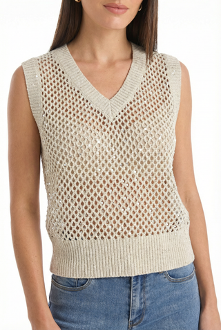 A woman wears the Addison Sequin Crochet Top - Pearl, a sleeveless open-knit sweater vest with a V-neck and ribbed hem, styled with blue jeans. The resort-ready outfit stands out against a plain white background.