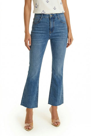 A person wearing Nicolette Cropped Jean - Medium Blue, high-waisted and slightly flared, paired with clear heeled sandals. The visible lower half is styled with a sleeveless white top featuring a small anchor print.