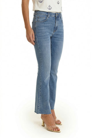 A person wears the Nicolette Cropped Jean in medium blue with frayed hems, a white patterned top, and clear-strap heeled sandals on a white background—effortless summer style.