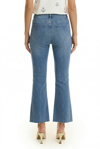 A person wearing the Nicolette Cropped Jean in medium blue, featuring a slightly flared cropped silhouette with frayed hems and beige heeled shoes, seen from the back against a white background—effortless summer style.