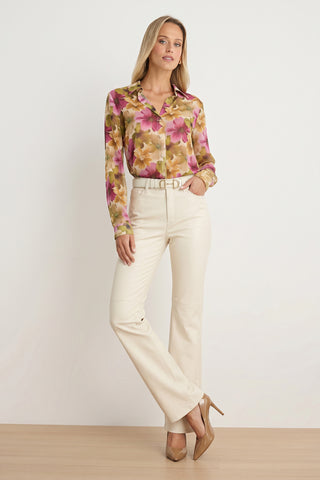 A woman stands against a plain wall, wearing the Ana Chiffon Blouse in a pink and yellow floral print. She pairs the versatile women's top with cream-colored belted pants and nude heels. With straight blonde hair, she strikes a relaxed, confident pose, one hand tucked into her pocket.