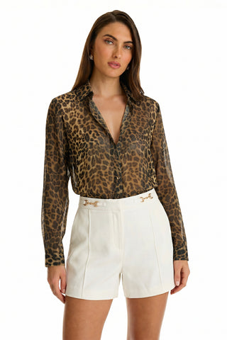 A woman wears the Ana Chiffon Blouse - Leopard, a sheer, long-sleeve leopard print top, tucked into high-waisted white shorts with gold chain accents against a plain white background.