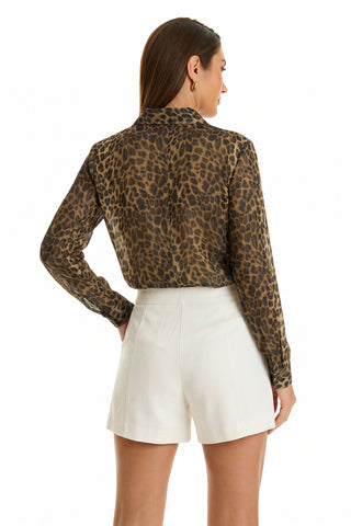 A woman with straight brown hair models the Ana Chiffon Blouse – Leopard, a long-sleeved, brown leopard print top, tucked into high-waisted white shorts, posing against a plain white background.