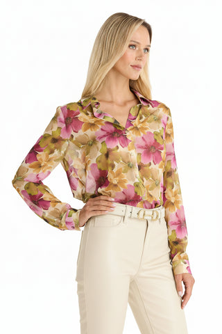 Woman wearing the Ana Chiffon Blouse - Floral Print, featuring sheer fabric and vibrant pink, yellow, and green florals, paired with high-waisted cream pants and a matching belt, standing with one hand on her hip.