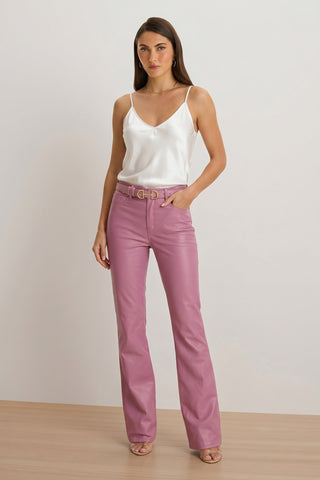 A woman with long straight hair and a neutral expression stands against a plain background wearing a white satin camisole, Aria Coated Flare Jean in mauve, and nude heeled sandals.