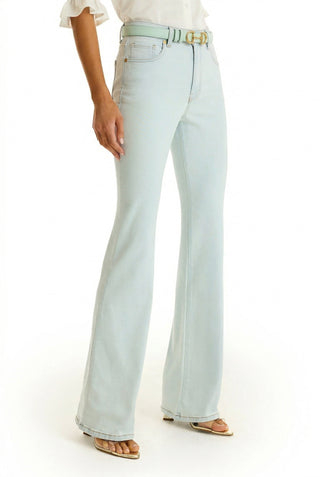 A woman wears the Aria Flare Jean - Cloud, a light wash high-rise fit with a matching belt, paired with a white blouse and open-toe heels, standing against a white background.