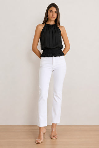 A woman stands against a plain background wearing the Betsy Halter Top in black, paired with high-waisted white jeans and clear heeled sandals. Perfect for summer fashion, her arms are relaxed at her sides and her hair is down.