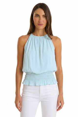 Woman facing forward in the Betsy Halter Top - Sky Blue, a feminine blouse with ruched waist and ruffle hem, paired with white pants against a plain white background—perfect for a summer look.