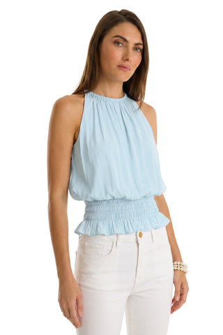 A woman wears the Betsy Halter Top - Sky Blue with high-waisted white pants, standing against a white background.