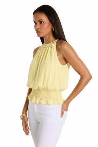 A woman models the Betsy Halter Top - Sunshine Yellow, a sleeveless, feminine top with a smocked waist, paired with white pants—an easy summer look against a plain white background.