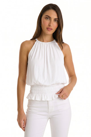 A woman models the Betsy Halter Top - White, featuring a gathered neckline and smocked waistband, styled with fitted white pants—an effortless summer look set against a plain light background.