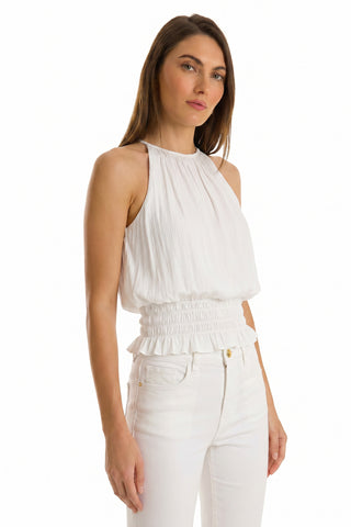 A woman models the Betsy Halter Top - White, a sleeveless, high-neck summer piece with a gathered waist, styled with high-waisted white jeans against a plain white background for an elevated resort look.
