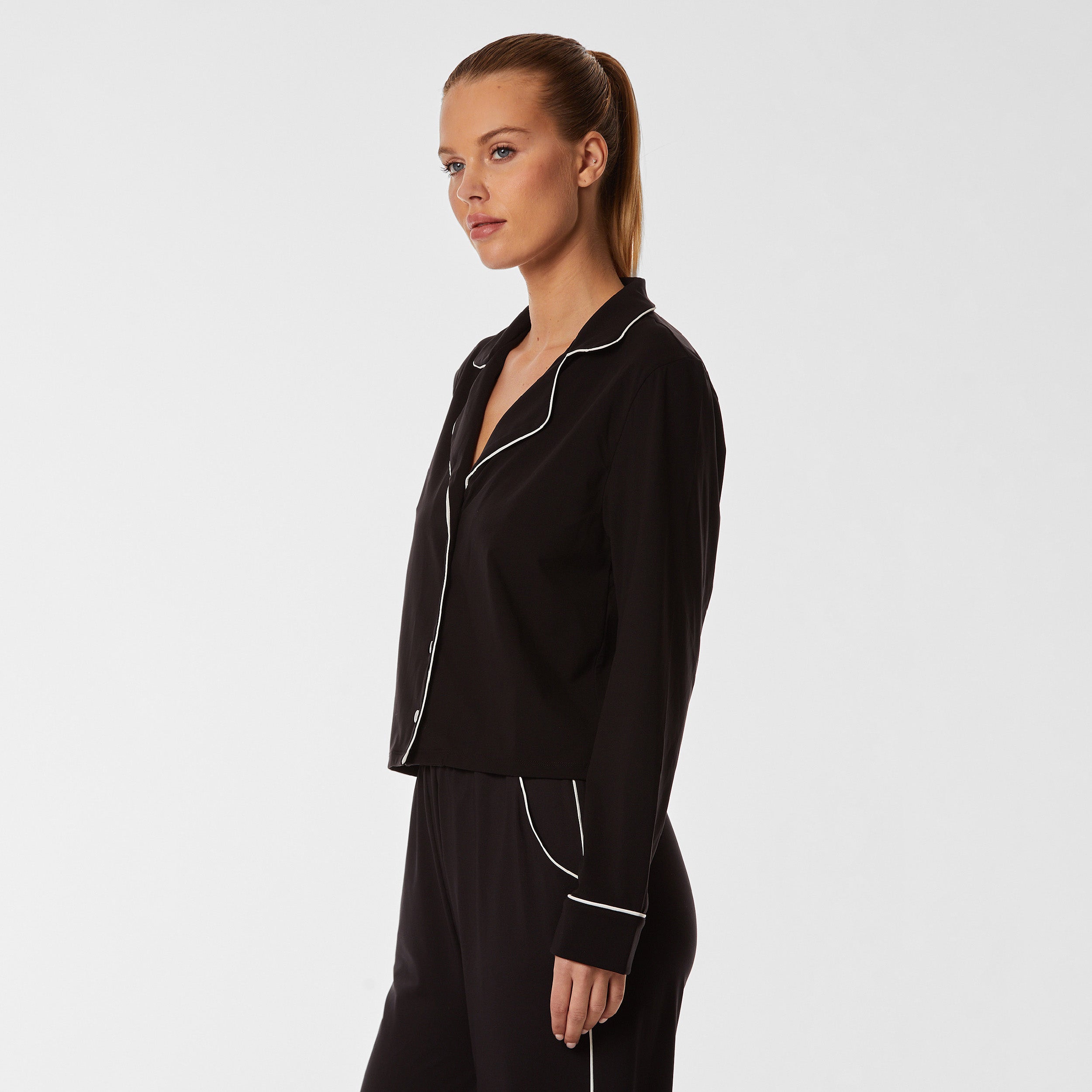 3/4 side view of woman wearing soft Black Pajama shirt with white piping detail and white buttons.