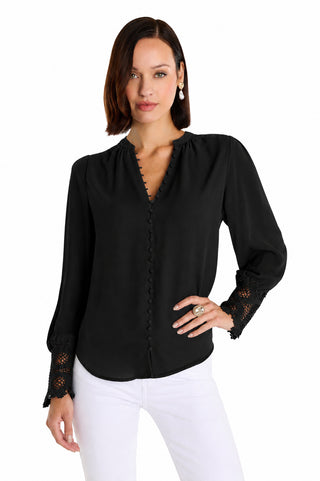 A woman wears the Blake Lace Sleeve Blouse in black, featuring long lace sleeves, button details, and lace cuffs, paired with white pants against a plain white background.