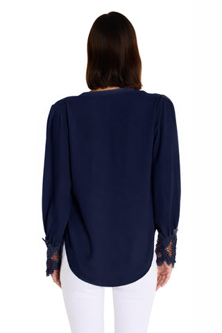 A woman with dark brown hair is seen from behind wearing the Blake Lace Sleeve Blouse in navy and white pants, standing against a plain white background.