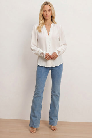 A woman stands indoors against a light background, wearing the Blake Lace Sleeve Blouse in white and blue jeans. She has long blonde hair, beige heeled sandals, and looks directly at the camera.