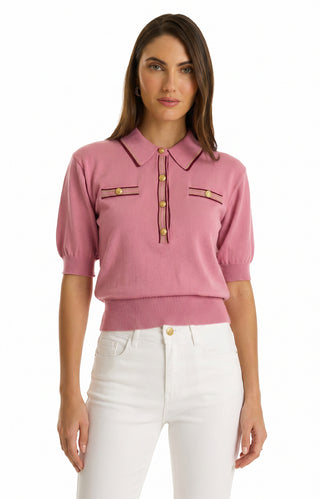 A woman in the Bobbi Polo Shirt - Dusty Rose, featuring a soft knit, collar, button placket, and chest buttons, pairs it with high-waisted white pants as she stands against a plain white background for a refined casual look.