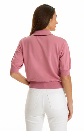 A woman with long brown hair, wearing a Bobbi Polo Shirt in Dusty Rose and white pants, stands facing away from the camera against a plain white background.