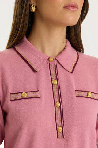 Wearing the Bobbi Polo Shirt - Dusty Rose, a woman showcases gold buttons, decorative trim, and two chest pockets. Her long brown hair and gold floral earrings complete her look.
