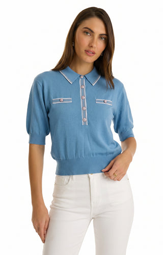 A woman wearing the ultra-soft knit Bobbi Polo Shirt - Serene Blue with embossed dome buttons and two chest pockets, paired with high-waisted white jeans, stands against a plain white background.