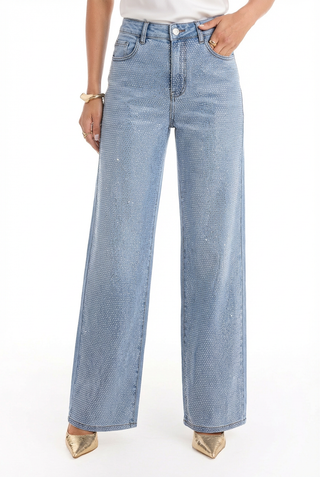 A person wears the Brynn Crystal Jean in medium blue, paired with a white top and gold pointed-toe shoes; only the lower half of the body is shown.