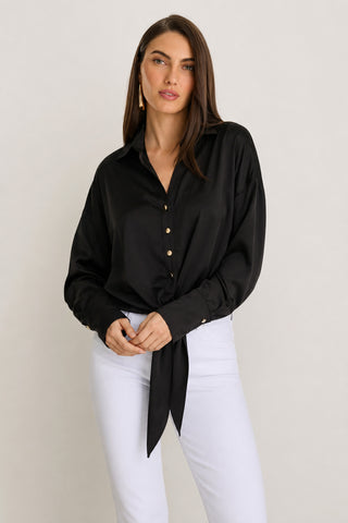 A woman wears the Cecilia Silk Tie-Front Blouse in black with white pants, standing against a plain light background and looking at the camera with a neutral expression.