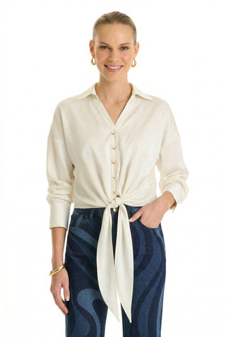 A woman smiles with one hand in her dark blue jeans pocket while wearing the Cecilia Silk Tie-Front Blouse in white, styled with gold hoop earrings and a gold bracelet.