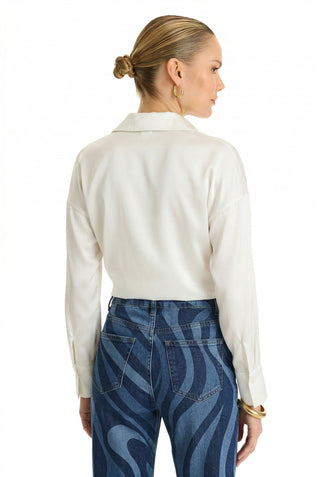 A woman with blonde hair in a low bun wears the Cecilia Silk Tie-Front Blouse in white and high-waisted blue jeans with a wavy pattern, standing with her back to the camera against a white background.