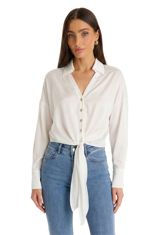A woman with long straight brown hair wears the Cecilia Silk Tie-Front Blouse in white, paired with blue jeans. She stands against a plain white background.