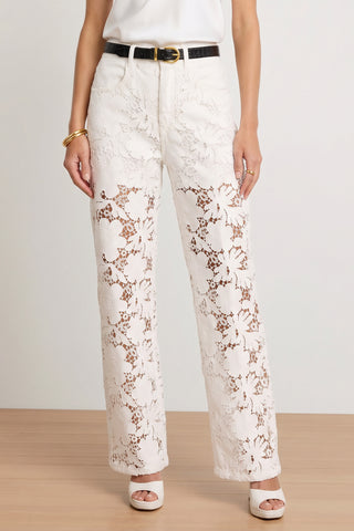 Wearing the Celeste High Rise Jean in white—a pair of high-waisted, wide-leg luxury statement jeans—styled with a black belt, gold bracelets, and white platform heels, a person stands on a wooden floor.