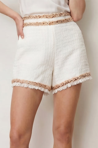 A person wears the Cheri Tweed Short - Pearl Multi, a high-waisted textured white summer short with beige trim and fringe details, paired with a tucked-in white top.