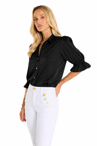 A woman with long blonde hair wears the Cindy Ruffle Sleeve Shirt in black, featuring gold buttons, paired with high-waisted white pants with gold buttons, standing against a plain white background.