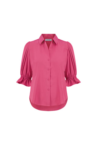 The Cindy Ruffle Sleeve Shirt in Petal Pink features a bright pink hue, short puffed ruffle sleeves, a collar, button-down front, gathered ruffled cuffs, and a subtle dolphin hem. Displayed on a plain white background.