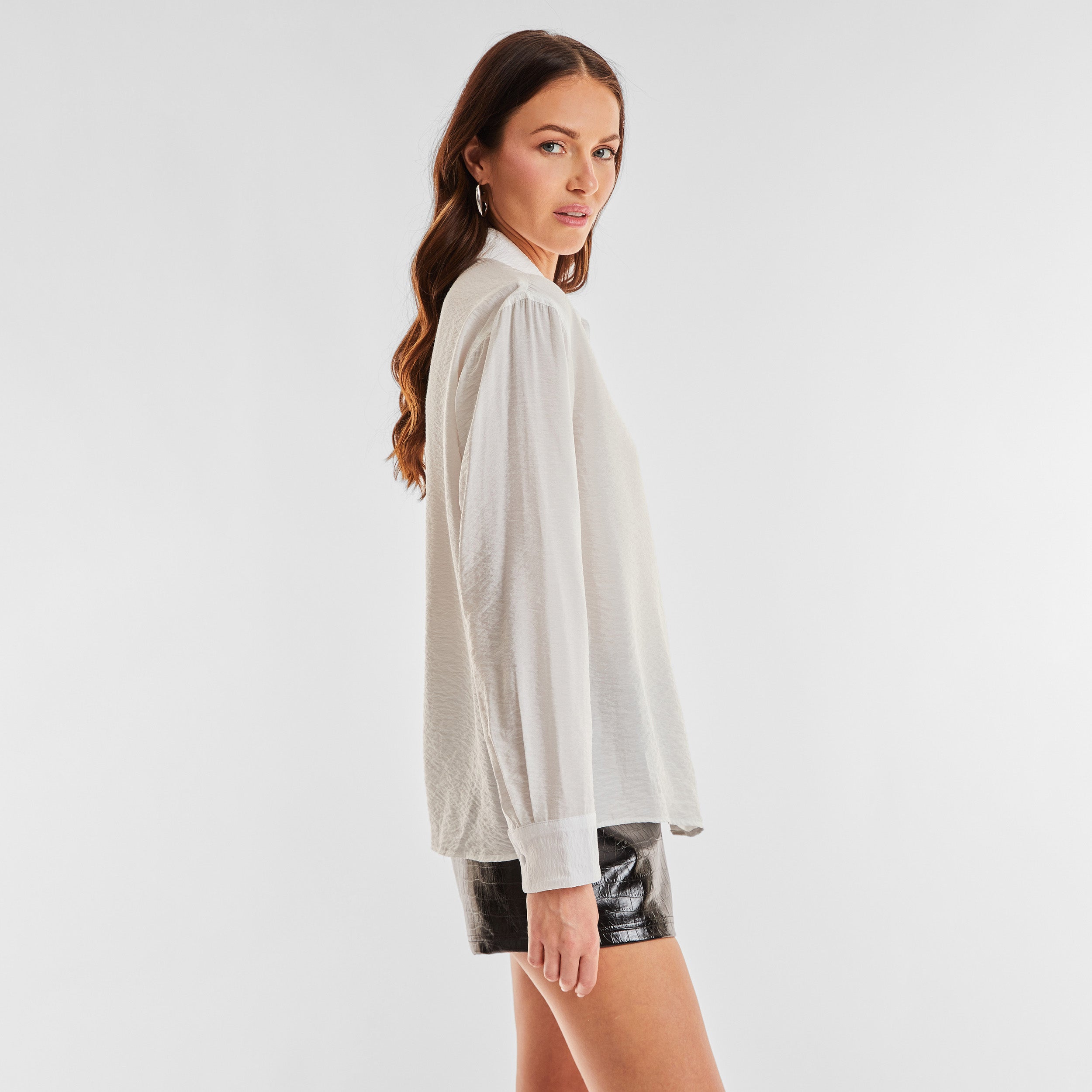 Side view of woman wearing sheer and textured long sleeve button up top.