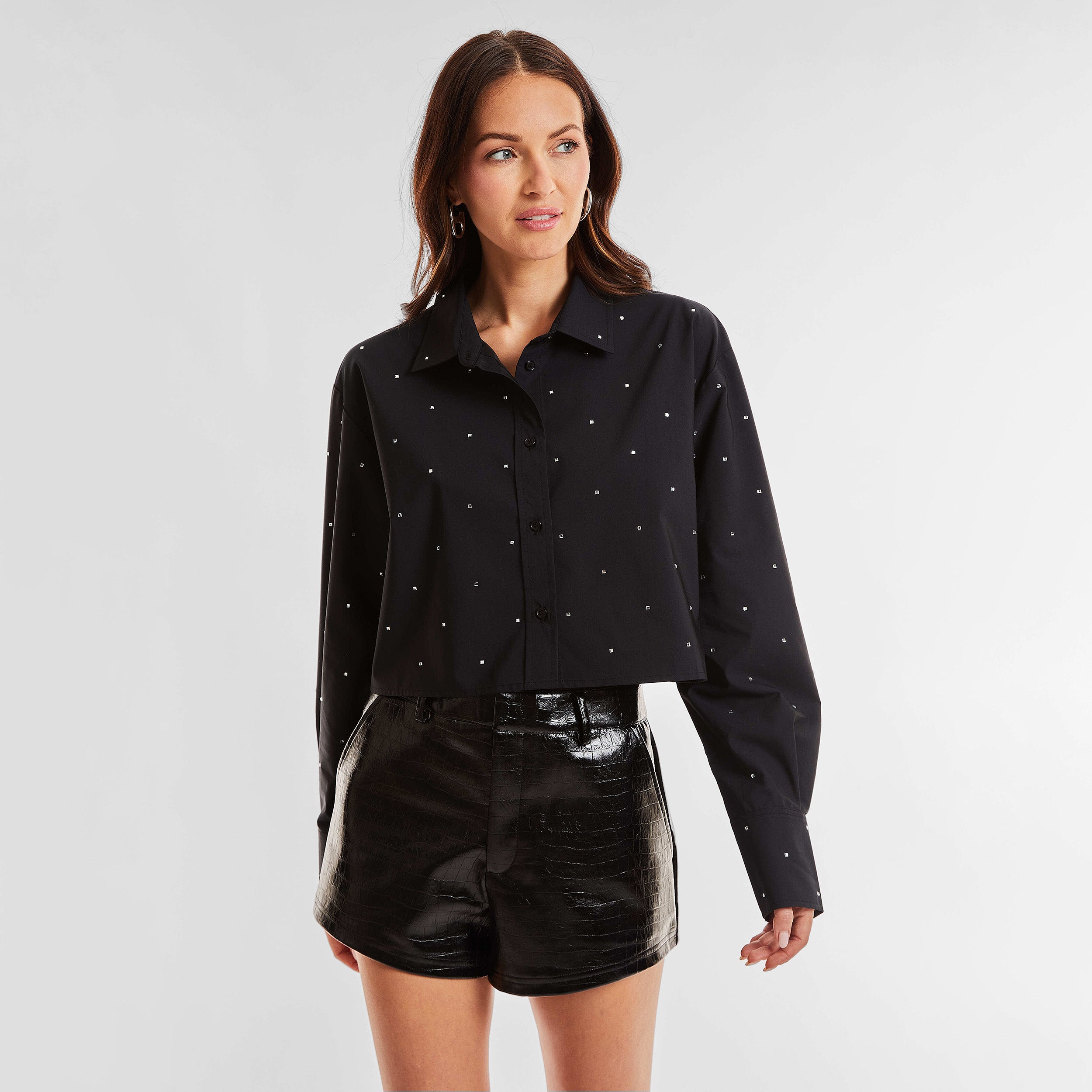 Front view of woman wearing a black cropped button down shirt with crystal embellishments and croco pattern embossed faux leather shorts.