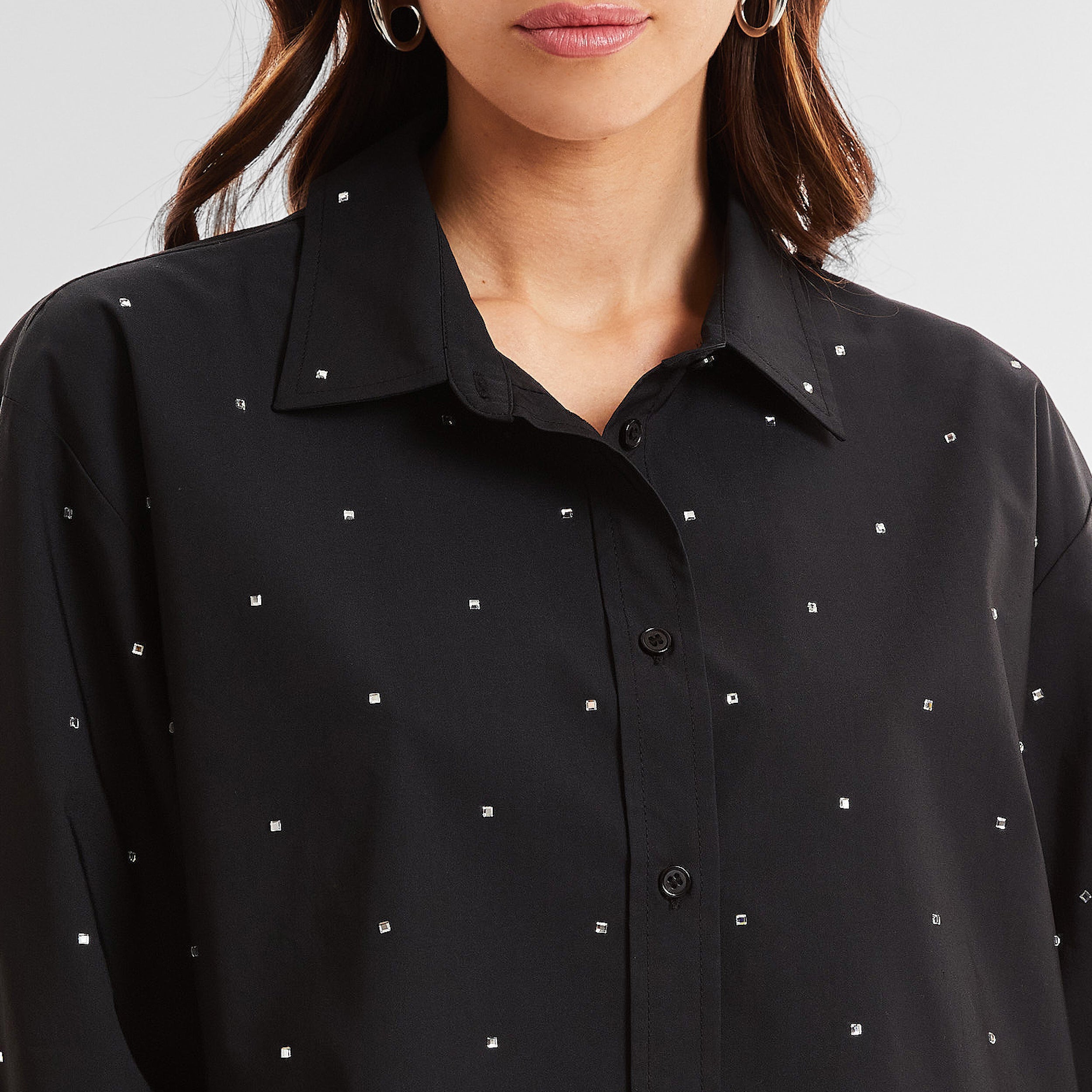 Close-up front view of woman wearing a black cropped button down shirt with crystal embellishments.