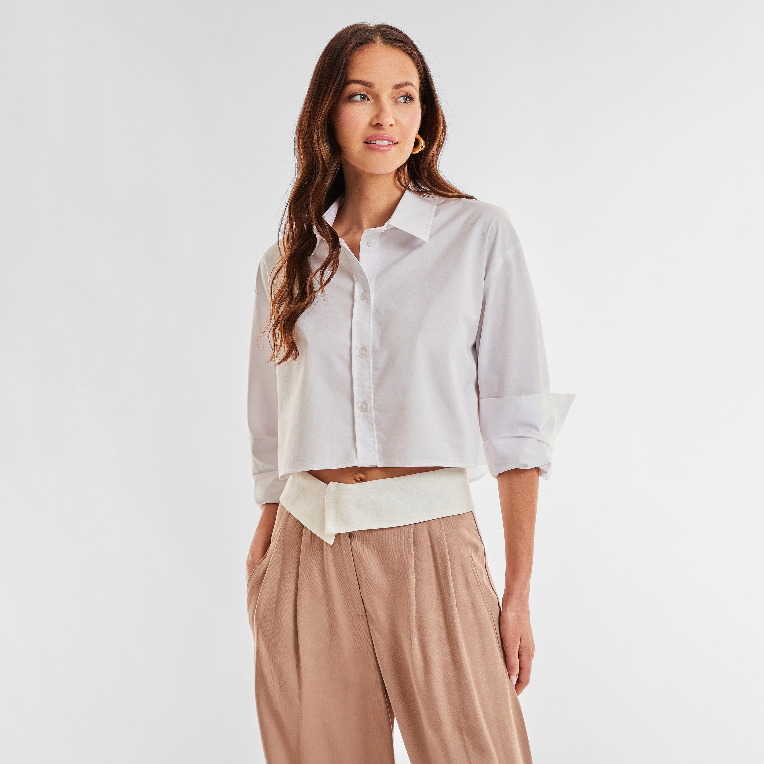 Front view of woman wearing a cropped white buttonup shirt and foldover waist mocha colored pant