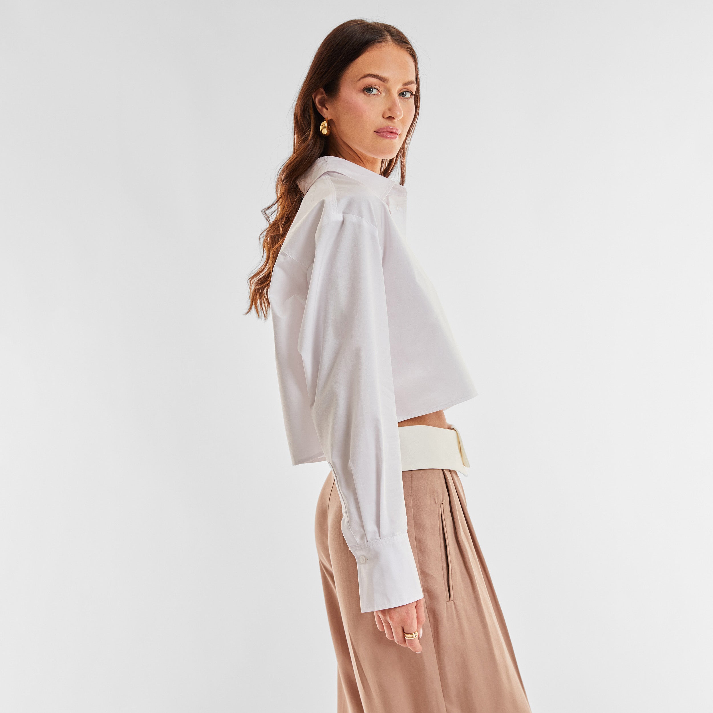 Side view of woman wearing a cropped white buttonup shirt and foldover waist mocha colored pant