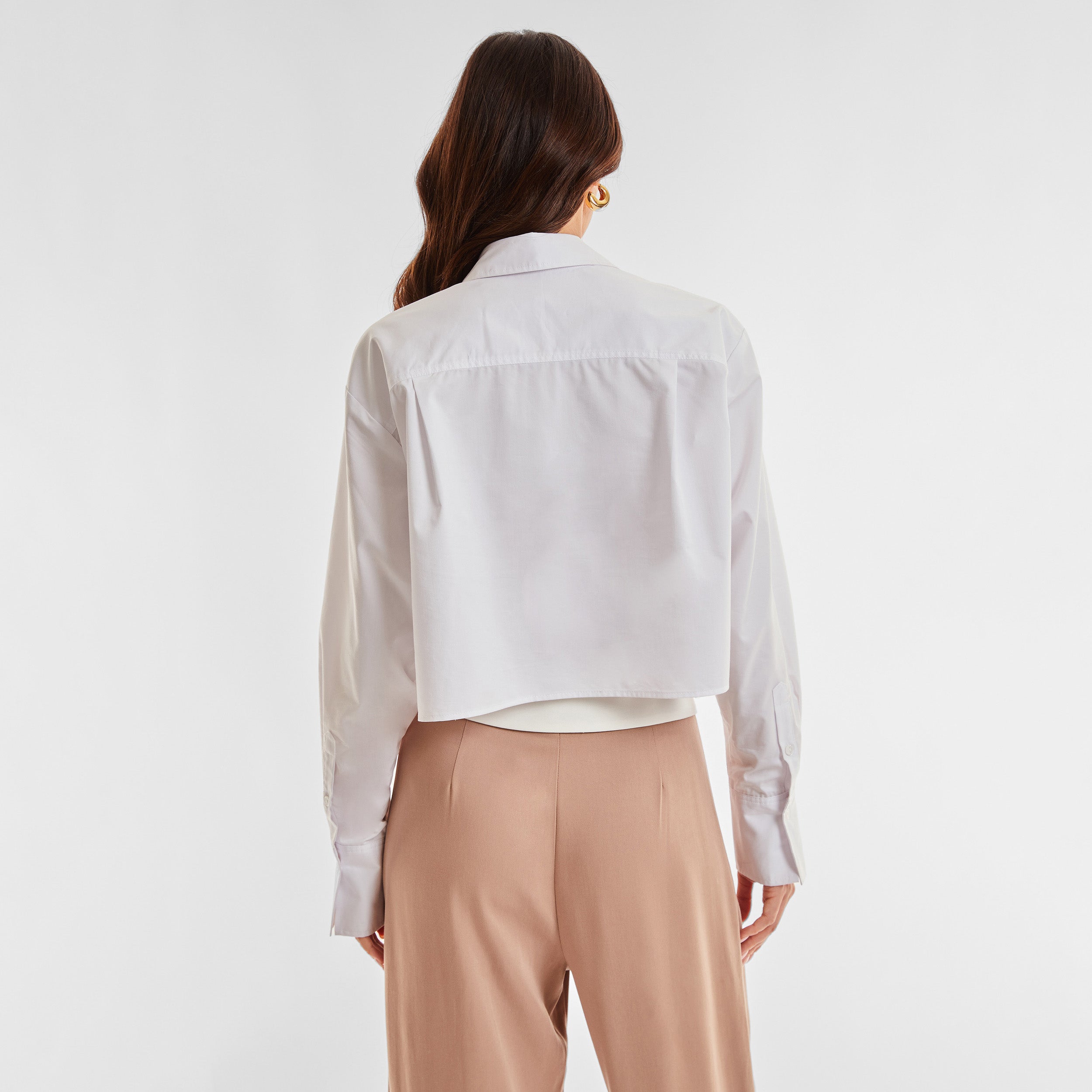 Rear view of woman wearing a cropped white buttonup shirt and foldover waist mocha colored pant